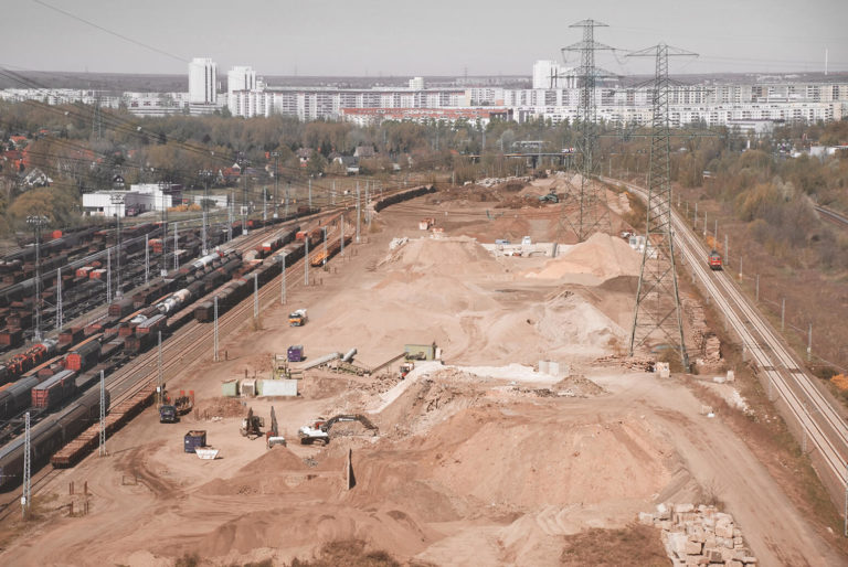 Luftaufnahme vom BTB Recyclinghof Berlin neben Bahngleisen, im Hintergrund das Neubaugebiet Hohenschönhausen