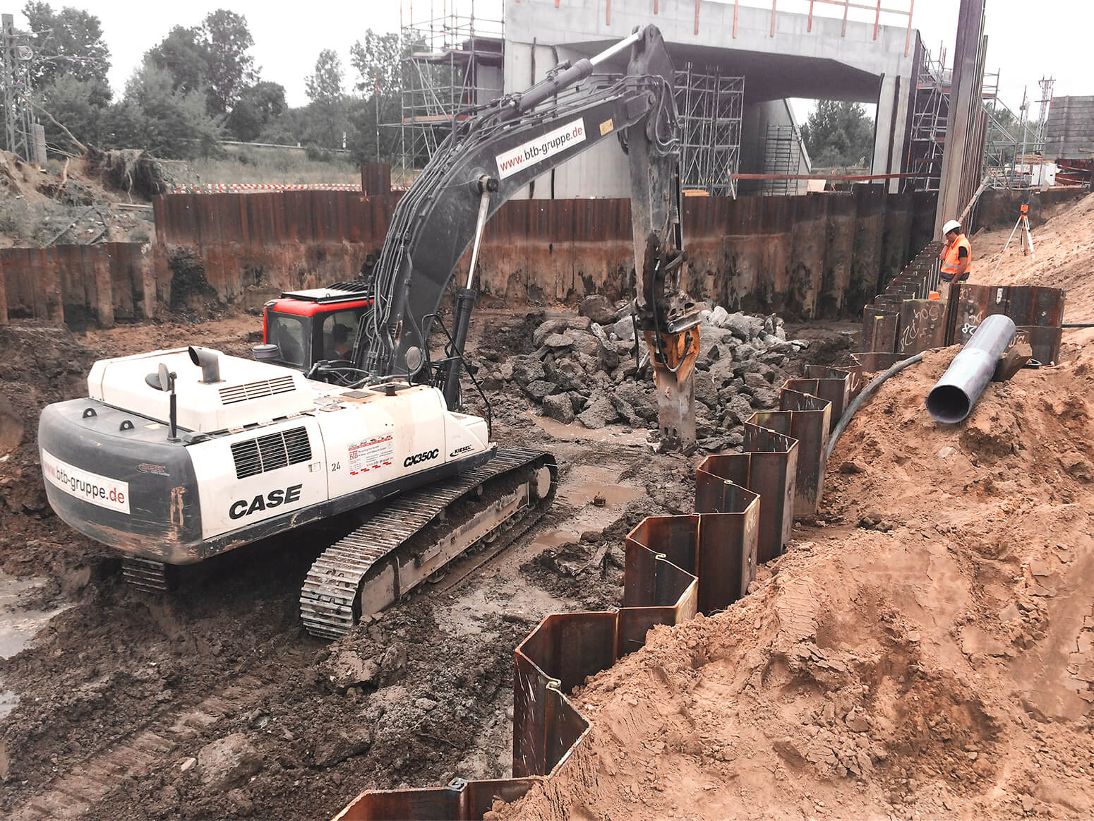 A heavy construction machine with a hammer demolishing an old embankment and old bridges