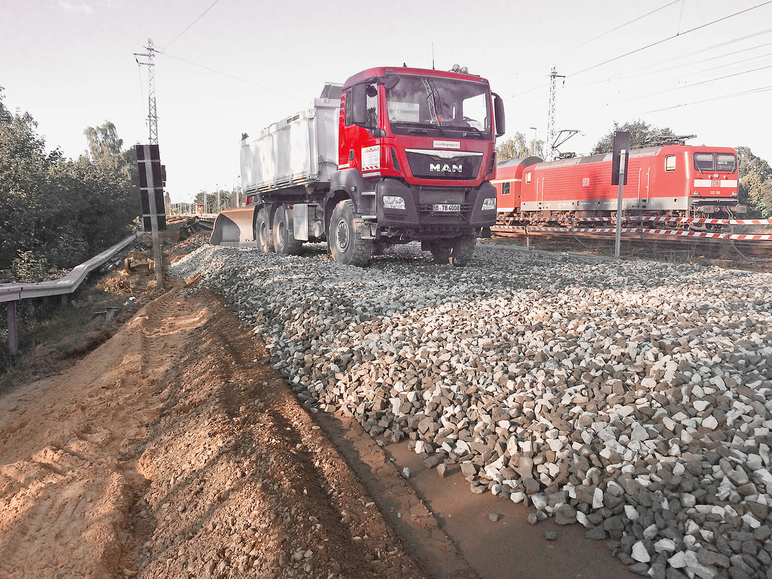 A BTB dumper truck on a freshly prepared gravel bed with a DB S-Bahn (city train) and railway tracks in the background