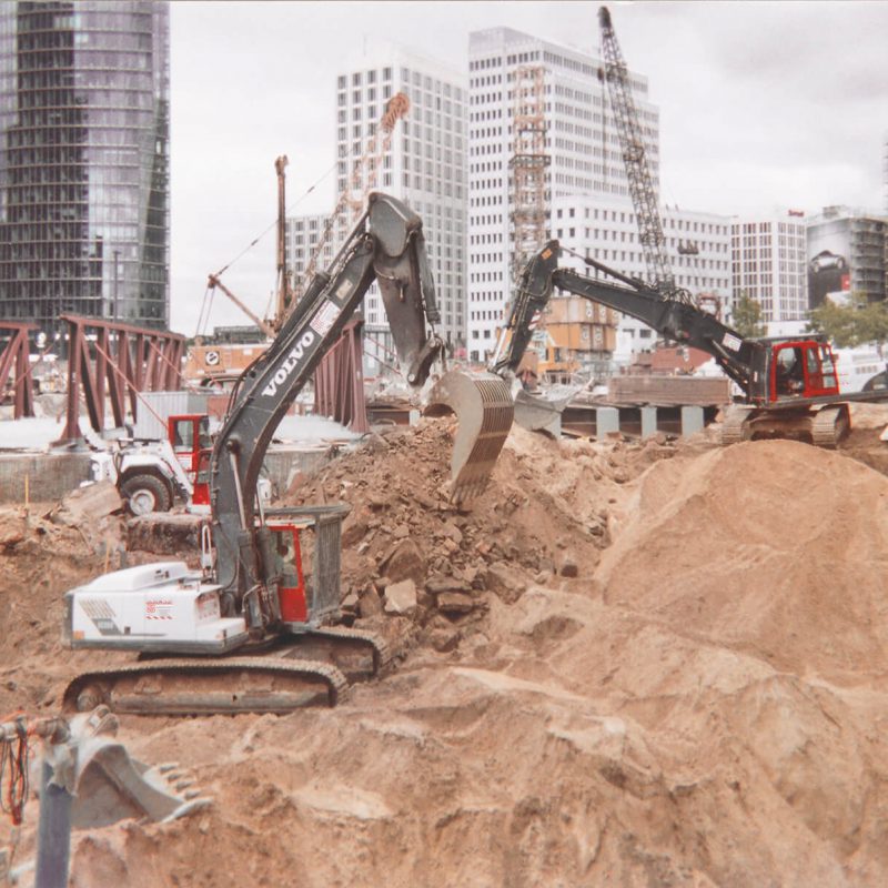 mehrere Bagger von BTB heben eine Baugrube am Potsdamer Platz in Berlin aus, im Hinterrund Kräne, das Beisheim Center und das DB Hochhaus