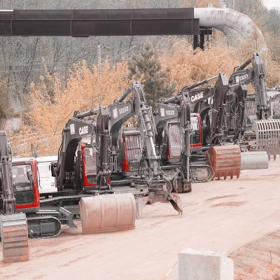 mehrere Baumaschinen von BTB mit verschiedenen Anbauteilen, Schaufeln und Gabeln stehen in einer Reihe, Im Hintergrund Bahngleise